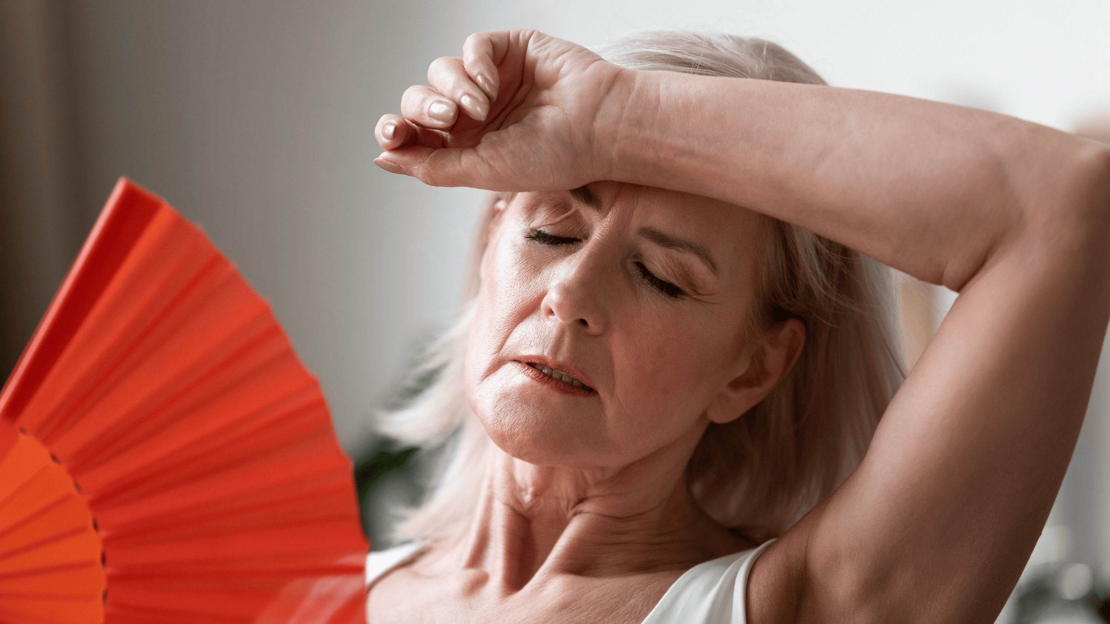 Woman fanning herself and wiping her forehead, appearing overheated and uncomfortable.
